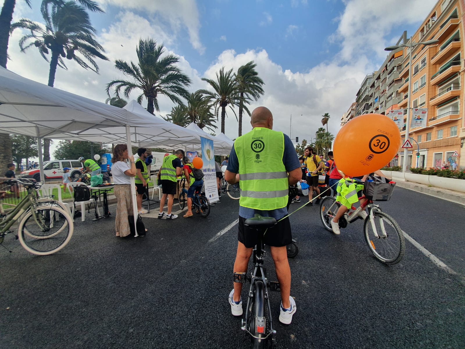 Participante con chaleco Ciudad 30 en la Ciclovía junto a puestos y palmeras